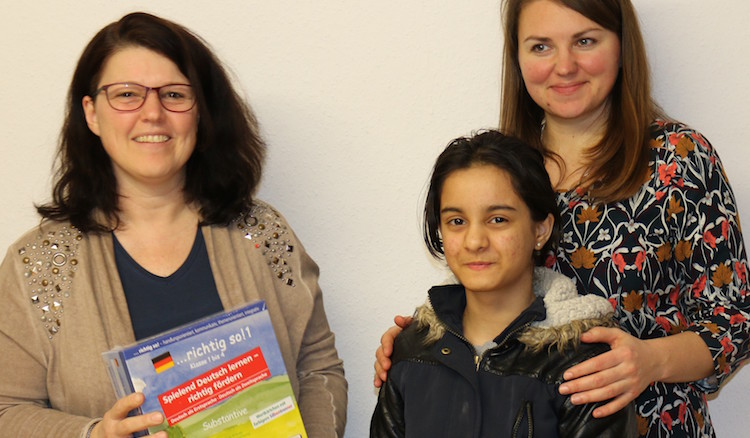 Ute Vogt überreicht der 10-jährigen Tina aus Afghanistan ein Sprachlernpaket mit Übungsheften und Lernkärtchen. Auch eine Betreuerin der Unterkunft freut sich mit.