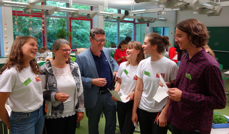 Die vier Mitglieder des Orga-Teams, mit T-Shirts mit Wappenaufdruck und Namensschild zeigen Ute Vogt und Stefan Kaufmann den Geschenke-Laden mit Selbstgebasteltem.