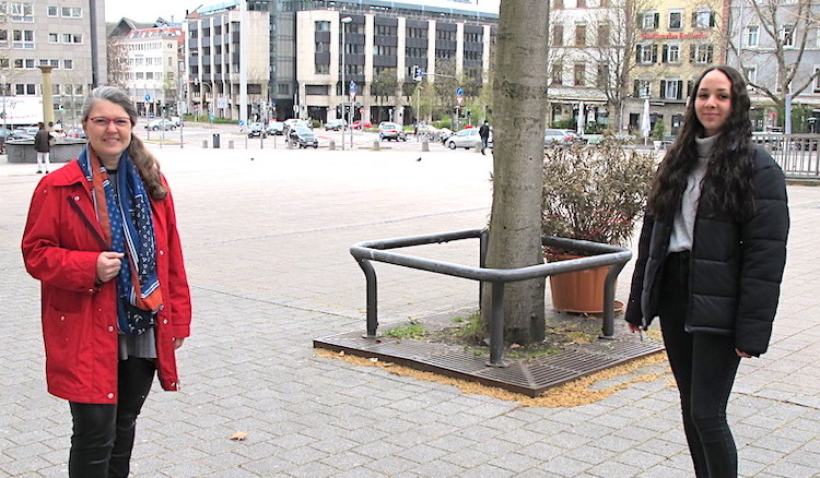 Ute in roter Jacke und Sanae in schwarzer stehen auf dem Wilhelmsplatz - im Hintergrund die Häuserzeilen